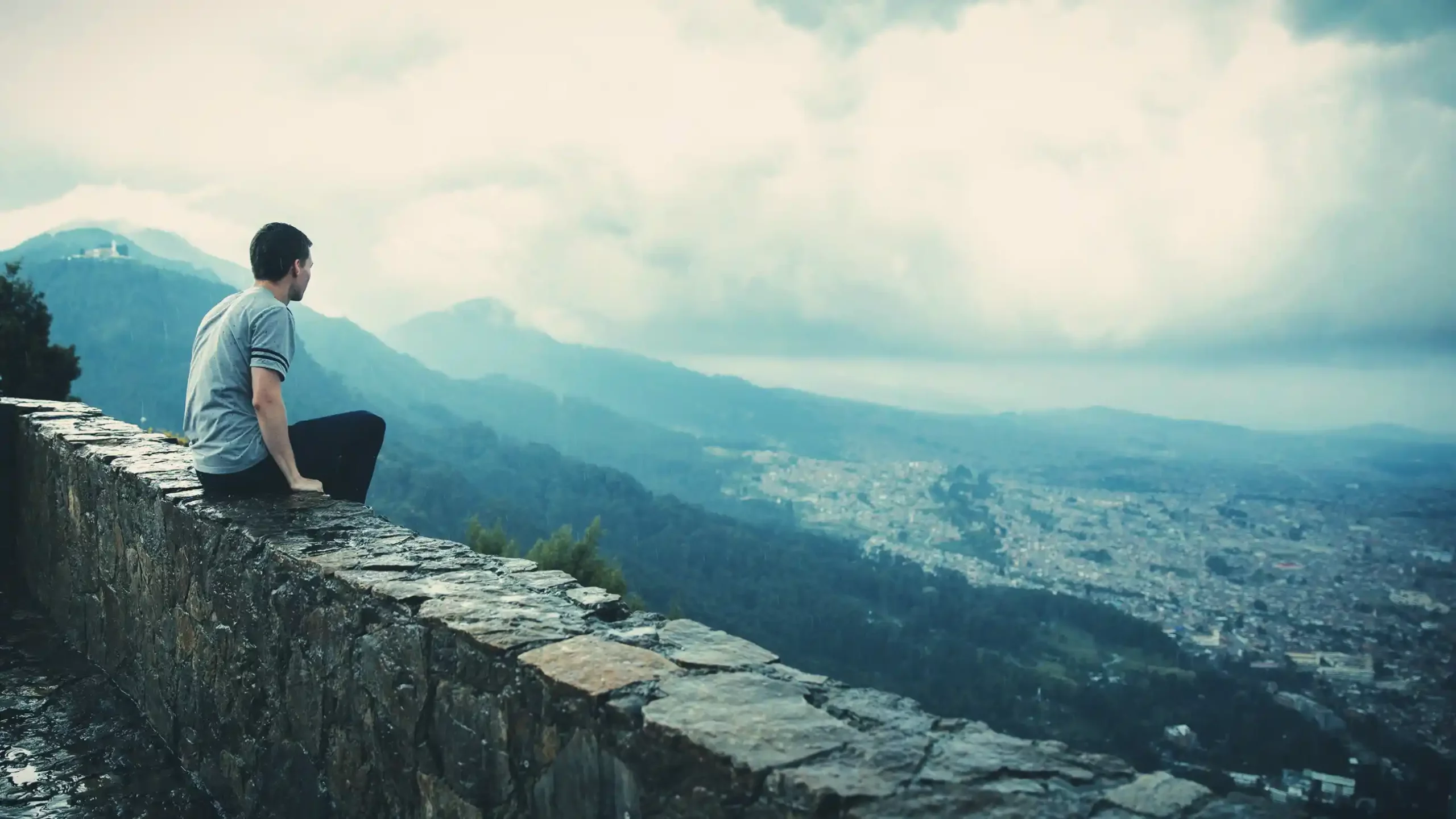 Man-sitting-on-rock-wall-and-overlooking-city