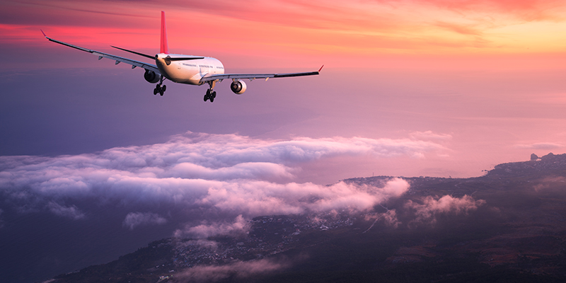 Airplane. Landscape with big white passenger airplane is flying in the red sky over the clouds at colorful sunset. Journey. Passenger airliner is landing at dusk. Business trip. Commercial plane