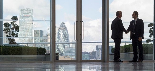 Businessmen handshaking in highrise office with urban city view, London, UK