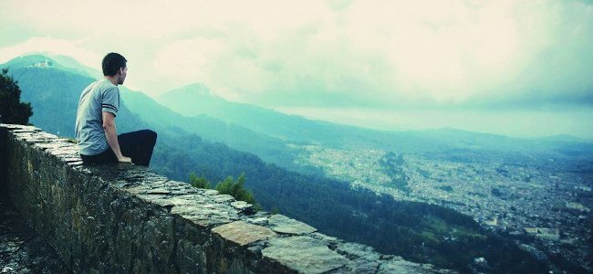 Man-sitting-on-rock-wall-and-overlooking-city