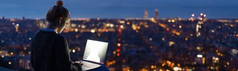 Young woman using laptop at dawn above the city, Barcelona, Spain