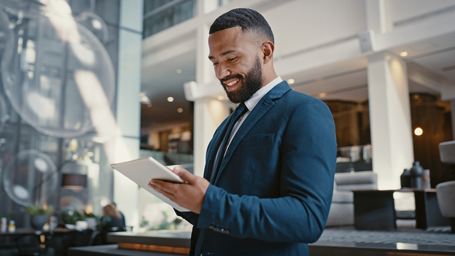 Demand360 solution A man wearing a suit in a smart hotel lobby looks down at a tablet device