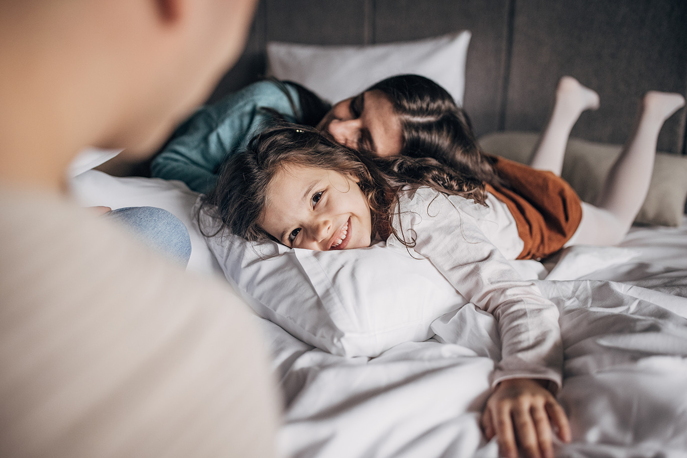 Three people husband and wife together in hotel room on bed with their little daughter they are on vacation