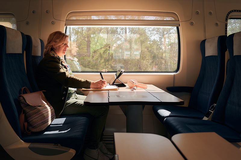 Woman works from a train with a tablet and a notebook.
