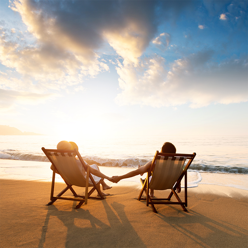A couple on a beach in deck chairs, holding hands