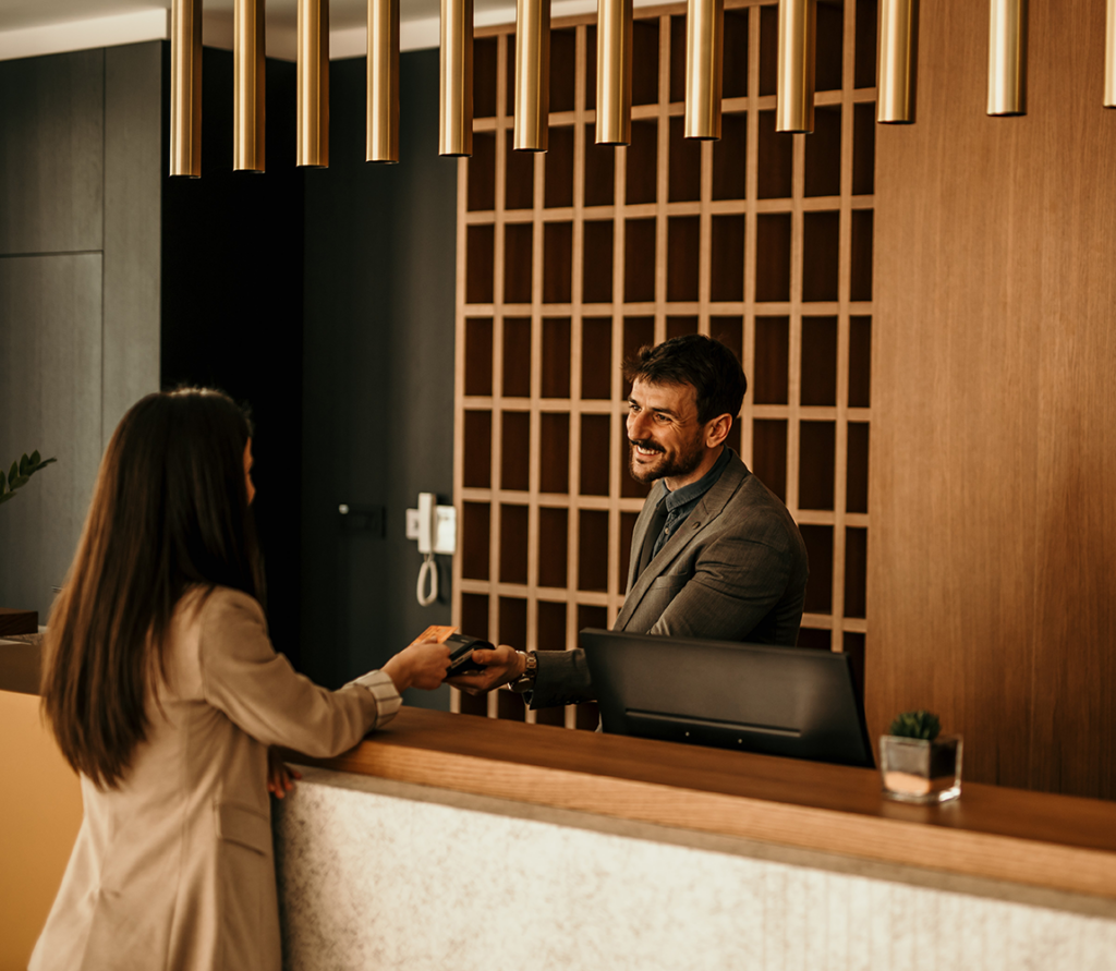 Smiling receptionist behind the hotel counter attending to a female guest. The concierge gives the documents to hotel guest 2
