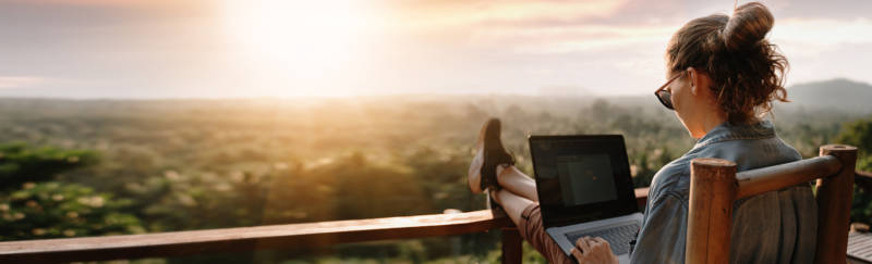 Young business woman working at the computer in cafe on the rock. Young girl downshifter working at a laptop at sunset or sunrise on the top of the mountain to the sea, working day.